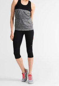 Canottiera sportiva nera e grigia con una parte superiore strutturata e parte inferiore liscia, abbinata a capri neri e sneaker grigie con lacci rossi.