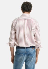 Een shirt met knopen, voorzien van verticale rode en witte strepen, met een relaxed fit en opgerolde mouwen, gecombineerd met blauwe spijkerbroek.