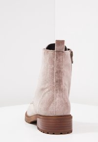 Bottines en suède rose clair avec un talon chunky marron, fermeture éclair sur le côté et une finition lisse et texturée.