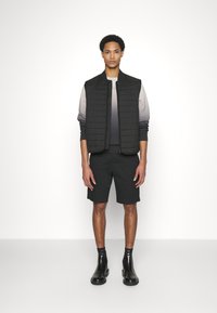 Gilet imbottito nero su una felpa grigia a gradiente, abbinato a pantaloni corti neri e stivaletti neri lucidi. Design semplice e silhouette aderente.
