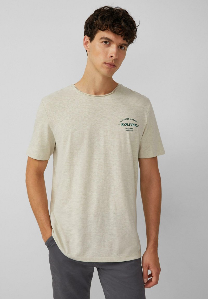 Helles beige T-Shirt mit kurzen Ärmeln aus einem weichen Material, das ein grünes Grafiklogo auf der linken Brust und einen Rundhalsausschnitt aufweist.