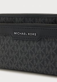 Πορτοφόλι Michael Kors σε μαύρο ύφασμα με χαρακτηριστικό μοτίβο μονόγραφου. Διαθέτει ασημί μεταλλικά στοιχεία και κλείσιμο με φερμουάρ. Λεπτομέρειες με λεία υφή.