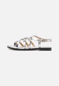 Sølvmetallic flate sandaler har flere stropper, syntetisk materiale, spennende detaljer og en teksturert såle.