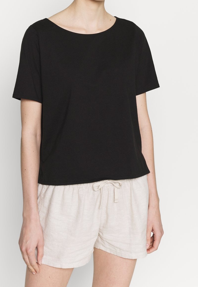 Černé tričko s krátkými rukávy a kulatým výstřihem, doplněné světle béžovými šortkami se stahovací šňůrkou a texturovaným vzorem.