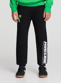 Pantaloni della tuta neri con grafica pixelata verde e scritta bianca "Minecraft" sulla gamba sinistra, realizzati in tessuto morbido con vestibilità comoda.