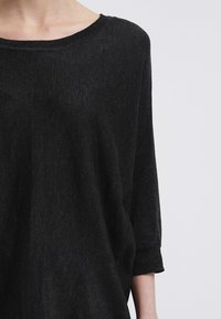 Maglia nera, con vestibilità morbida, colletto ampio e maniche a tre quarti. La texture sembra morbida con una leggera lucentezza.