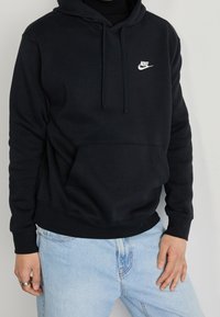 Svart huvtröja med en framficka, justerbar dragsko på huvan och vit Nike-logotyp på bröstet. Mjuk tygtextur.