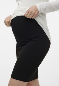 Pantaloni scurți de maternitate negri, cu un design strâmts, asortați cu un top alb cu mâneci lungi. Materialul pare elastic și se conturează pe corp.