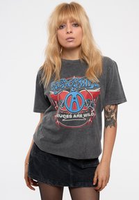 Gray graphic t-shirt featuring a blue and red design with text. Short sleeves and a relaxed fit. Worn with a dark denim skirt.