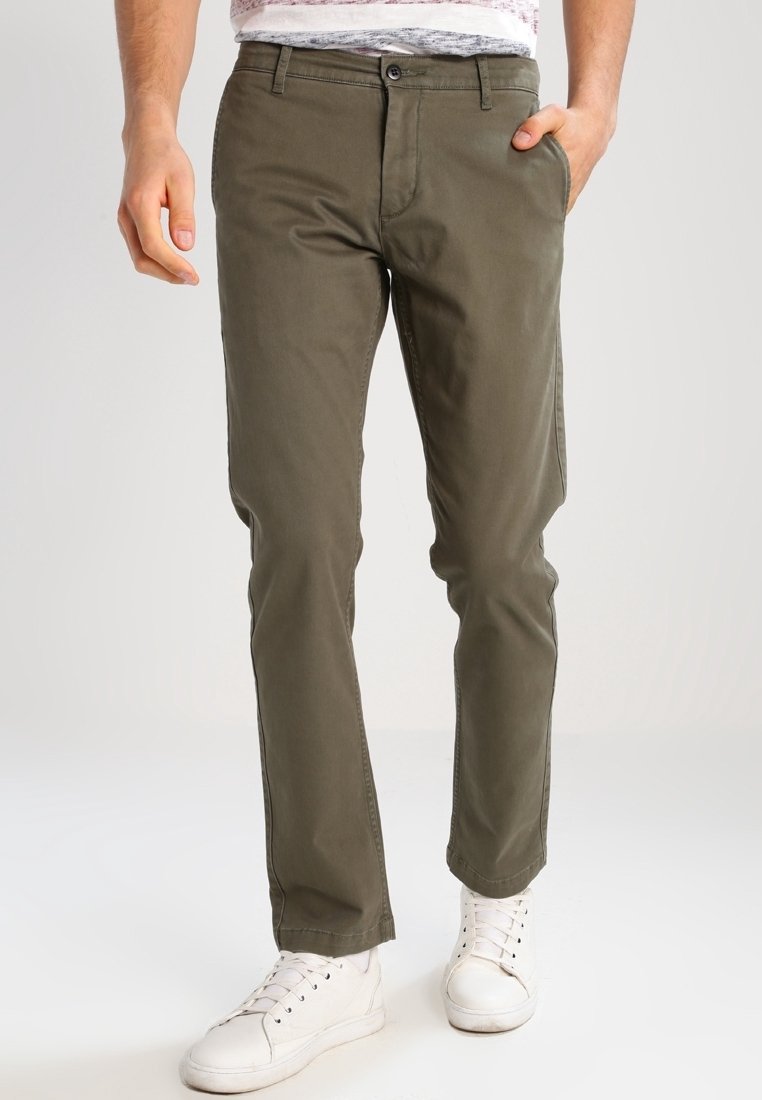 Chinos vert olive en coton, avec une coupe droite, des poches avant et une fermeture à bouton. Associés à des baskets blanches.