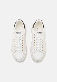 Weiße Ledersneaker mit goldenen Ösen, flachen Schnürsenkeln und einem strukturierten schwarzen Muster an der Ferse. Branding sichtbar auf der Zunge und der Seite.