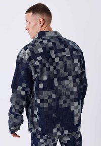 Chaqueta a cuadros en azul oscuro y gris, hecha de mezclilla, con un corte relajado, cuello puntiagudo y patrones cuadrados de estilo parche.