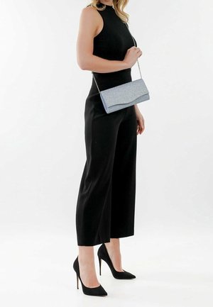 Clutch azul claro con una superficie texturizada y solapa curvada, con cadena adjunta. Combinado con una blusa sin mangas negra y pantalones culotte.
