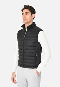 Gilet puffa nero con colletto alto, chiusura frontale con zip e due tasche laterali. Presenta una texture trapuntata e un materiale leggero.