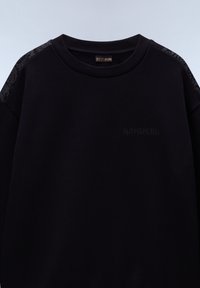 Černá mikina se žebrovaným kulatým výstřihem, texturovanými detaily na ramenou a embosovaným logem značky na hrudi. Hladký materiál.