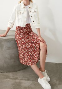 Veste en denim blanche, à manches courtes, couleur bleu délavé ; jupe midi fleurie marron, fente latérale ; baskets blanches. Textures lisses et design décontracté.