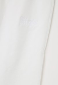 Witte katoenen stof met een zachte textuur, voorzien van een subtiele, witte reliëf 'Utopia' logo aan de zijkant. Eenvoudig, strak ontwerp.