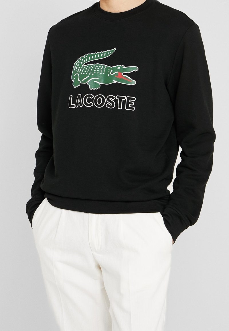 Černá mikina s dlouhými rukávy, s zeleným logem krokodýla a bílým textem "LACOSTE". Měkký materiál a volný střih.