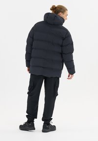 Schwarze Pufferjacke mit Kapuze, mit einem gesteppten Design und elastischen Bündchen, kombiniert mit schwarzen Cargo-Hosen und sportlichen schwarzen Schuhen.