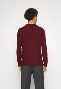 Śliwkowy sweter z długim rękawem, okrągłym dekoltem i ściągaczami na rękawach, wykonany z miękkiej tkaniny. Posiada subtelny detal z logo z boku.