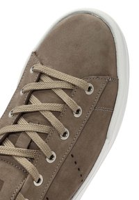 Zapatilla de ante marrón con punta redonda, cordones beige, ojales plateados y suela de goma blanca. Presenta costuras y perforaciones en el lateral.