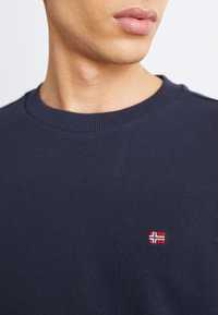 Felpa blu navy realizzata in tessuto morbido, con colletto a coste e una piccola bandiera norvegese ricamata sul petto.