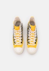 Höga sneakers med en gul canvasöverdel, svarta djurmönsteraccenter, vita snörningar och en blank vit gummitå.