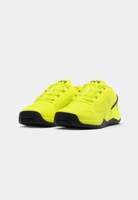 Neon gele sport schoenen met een mesh bovenkant, zwarte rubberen zool en vetersluiting met logo-accenten op de tong en zijkant.