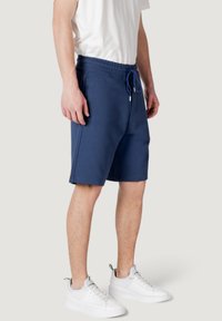 Pantalones cortos azul marino con cintura ajustable y bolsillos laterales, hechos de una tela suave; combinados con zapatillas blancas.