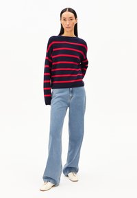 Marine gestreepte sweater met rode horizontale strepen, relaxte pasvorm, ronde halslijn; gecombineerd met lichtblauwe wijde jeans en crèmekleurige schoenen.