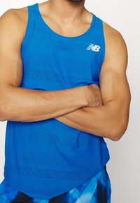 Blå atletisk linne med en strukturerad design och horisontella ränder samt en vit logotyp. Tillverkat av lätta material, utan ärmar.