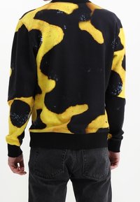 Sudadera negra con un audaz patrón abstracto en amarillo y negro, de mangas largas y dobladillo acanalado. Tejido texturizado.