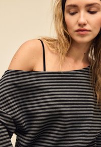 Siv črno črtast top z odkritimi rameni in ohlapnim krojem. Ima tanke črne naramnice, mehko teksturo in vzorec vodoravnih črt.
