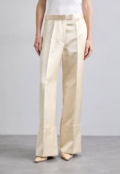 Beige satin vide bukser med høj talje, der har frontfolder og en karakteristisk splitkant detalje.