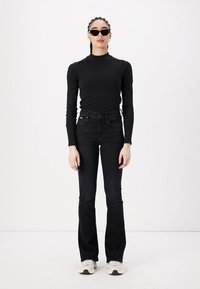 Black ribbed long-sleeve top paired with high-waisted black flared jeans. Wearing dark sunglasses. Shoes are light-colored with dark accents.