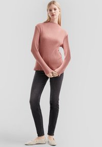 Rosa geripptes langärmliges Oberteil, kombiniert mit schwarzen Skinny-Jeans und hellen Ballerinas mit Nietenakzenten. Einfaches, tailliertes Design.