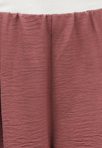 Κοντινό πλάνο υφής από κόκκινο-καφέ ύφασμα με ραφή που συγκεντρώνεται στο επάνω μέρος κάτω από λευκό ριμπ ύφασμα.