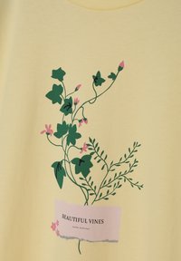 Žlutá bavlněná košile s zeleným botanickým potiskem a růžovými akcenty, na pastelové etiketě s nápisem "KRÁSNÉ VÍNY".