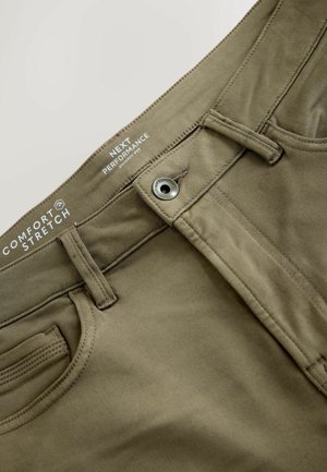 Nærbillede af olivengrønne skinny fit bukser med komfortstretchstof, synlig knap, bæltesløjfer og syninger på frontlommen.