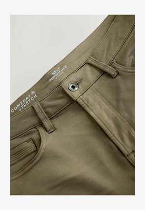 Detailní záběr na olivově zelené skinny fit kalhoty z pohodlné strečové látky, viditelný knoflík, poutka na pásek a prošívání předních kapes.