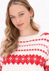 Strickpullover in Creme mit roten geometrischen Mustern, einschließlich Rautenformen. Besitzt einen weiten Halsausschnitt und gerippte Bündchen.