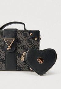 Fekete vászontáska mintás textúrával, arany színű fém kiegészítőkkel, háromszög alakú logótáblával, valamint hozzákapcsolt fekete szív alakú erszénnyel.