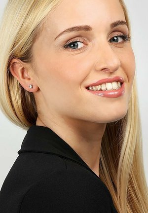 Silberne Steckerohrringe mit klaren Edelsteinen, die ein quadratisches Design aufweisen. Getragen von einer Person mit glattem blonden Haar, die ein schwarzes Blazer trägt.