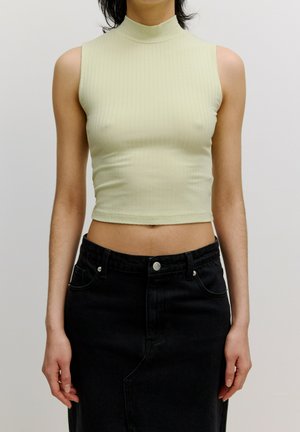Lichtgroene geribbelde mouwloze top met een mock neck, in combinatie met een hoog waisted zwarte denim rok met een split aan de voorkant en zilveren knoopdetails.