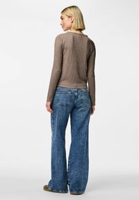 Brun, ribbad långärmad topp ihop med högmidjade, vida blå jeans. Jeansen har en klassisk femficksdesign med synliga sömnadsdetaljer.