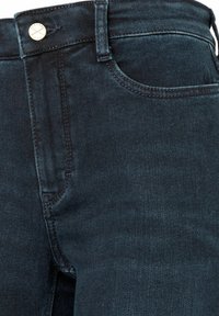 Dunkelblaue Jeans aus Denim mit glatter Oberfläche, ausgestattet mit einem silbernen Knopf und einem traditionellen Taschendesign auf der Vorderseite.