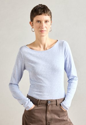 Light blue long-sleeve shirt with a wide neckline, paired with brown pants. Material appears soft and slightly textured.