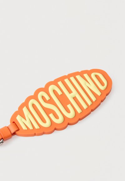 Πορτοκαλί λαστιχένιο μπρελόκ με ανάγλυκτο κείμενο "MOSCHINO" σε κρεμ απόχρωση και προσαρτημένο πορτοκαλί δερμάτινο λουράκι.