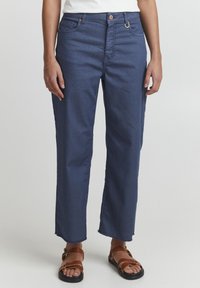 Jeans de mezclilla azul oscuro con corte recto, dobladillo deshilachado, diseño de cinco bolsillos y botones y herrajes de cobre en contraste.