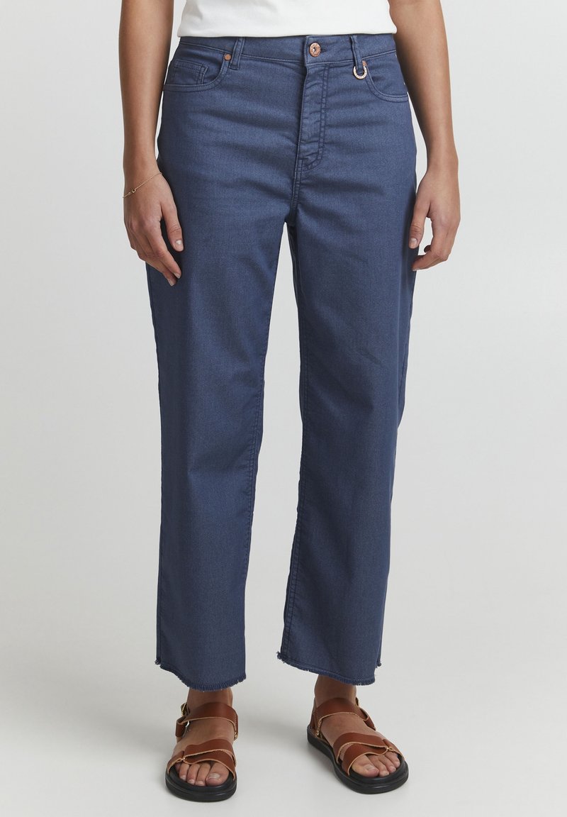 Jeans de mezclilla azul oscuro con corte recto, dobladillo deshilachado, diseño de cinco bolsillos y botones y herrajes de cobre en contraste.
